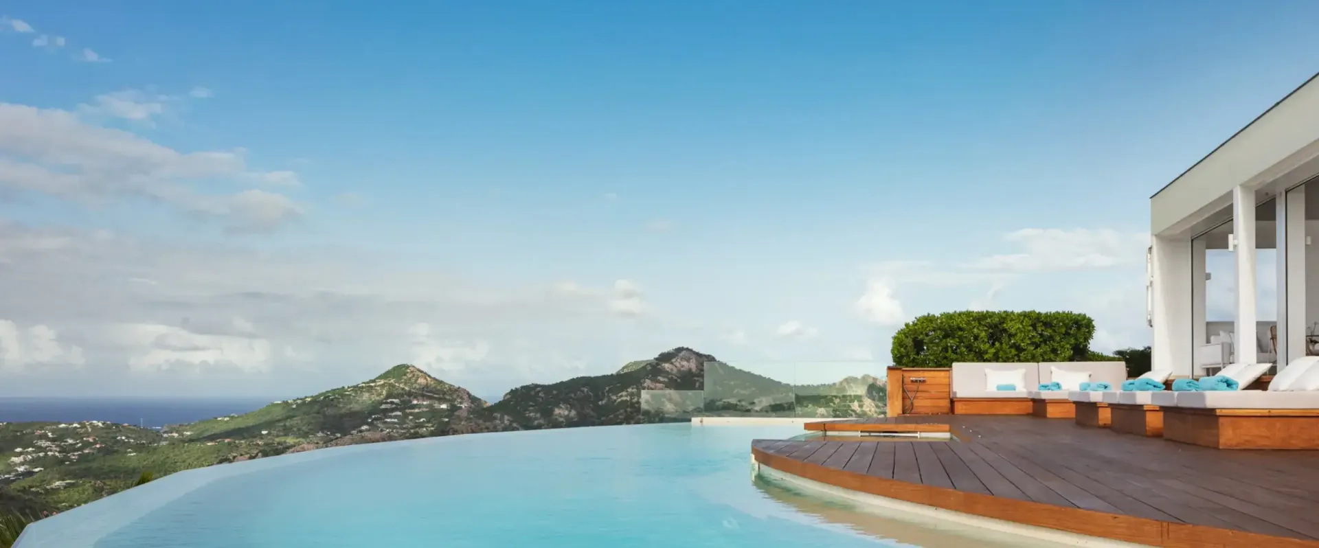 Ocean side luxury white villa with lounge seating next to an infinity pool with st barth hillside in the background