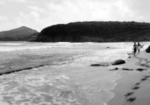 Two surfers walk out to a cliff side break.